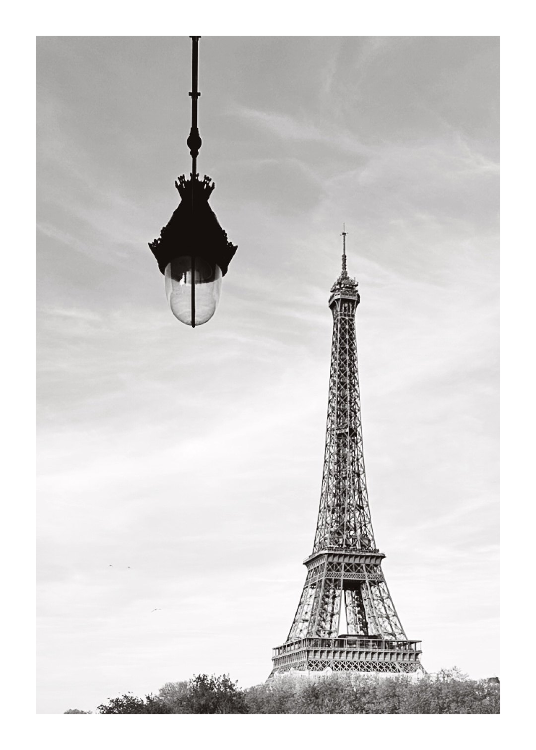 Black-and-white photo of the Eiffel Tower in the distance, with an ornate street lamp hanging in the foreground